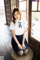 A woman in a school uniform sitting on a wooden floor.