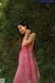 A woman in a pink dress standing in the woods.