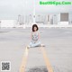 A woman sitting on the ground in a parking lot.