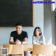 A man and a woman sitting at a table in front of a blackboard.