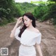 A woman in a white top and skirt standing on a dirt road.