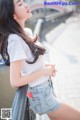 A woman in a white shirt and denim shorts leaning against a railing.