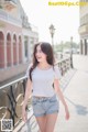 A woman in a white shirt and denim shorts walking down a sidewalk.