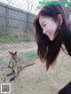 A woman standing next to a kangaroo in a fenced in area.