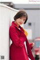 A woman in a red coat leaning against a wall.