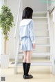 A woman in a blue and white school uniform standing in front of a staircase.