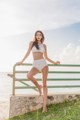 A woman in a white bikini standing on a railing by the water.