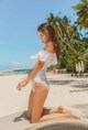 A woman in a white one piece swimsuit sitting on a beach.