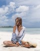 A woman sitting on a beach with a straw hat and sunglasses.