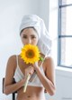 A woman with a towel wrapped around her head holding a sunflower.