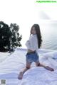 A woman sitting on top of a bed next to the ocean.