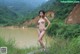 A naked woman standing on a log by a lake.