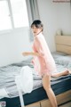 A woman in a pink robe is standing on a bed.