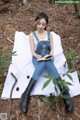 A woman sitting on a blanket in the woods reading a book.