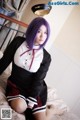 A woman with purple hair sitting on a bed.