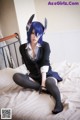 A woman with blue hair sitting on a bed.