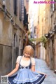 A woman in a blue and white dress is walking down a narrow street.