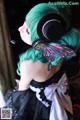 A woman with green hair wearing headphones and a black dress.