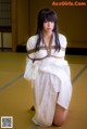 A woman in a white kimono is tied up on the floor.