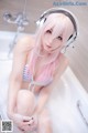 A woman with pink hair sitting in a bathtub with headphones on.