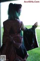 A woman with green hair standing in front of a window.