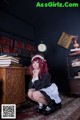 A woman in a maid outfit sitting on the floor in front of a bookcase.