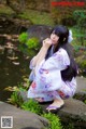 A woman in a kimono sitting on a rock by a pond.