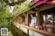 A woman in a blue dress standing on a porch next to a pond.