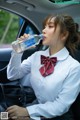 A woman sitting in a car drinking water from a bottle.