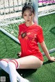 A woman in a red shirt and white socks sitting on a soccer field.