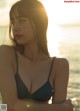 A woman in a black bikini sitting on the beach.