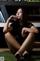 A woman sitting on the grass in front of a bookshelf.