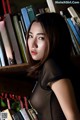 A woman leaning against a bookshelf full of books.