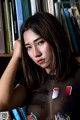 A woman leaning against a bookshelf in front of a bookcase.