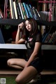 A woman sitting on the grass in front of a bookshelf.