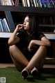 A woman sitting on the grass in front of a bookshelf.