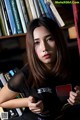 A woman standing in front of a bookshelf holding a book.