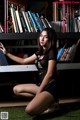 A woman sitting on the grass in front of a bookshelf.