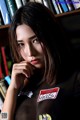 A woman in a black shirt sitting in front of a bookshelf.