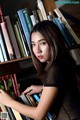 A woman leaning against a bookshelf full of books.