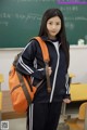 A young woman standing in front of a blackboard holding a backpack.