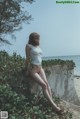 A woman in a white tank top sitting on a wall by the ocean.