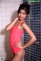 A woman in a pink bathing suit posing in a bathroom.