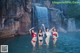 A group of women standing in the water near a waterfall.