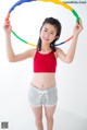 A young woman in a red top and gray shorts holding a hula hoop.