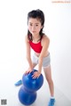 A young girl in a red top and gray shorts holding a blue ball.