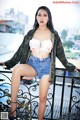 A woman in shorts and a camo jacket posing on a balcony.