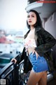 A woman in a camo jacket and denim shorts posing on a balcony.