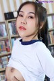 A woman in a white shirt is posing in front of a bookshelf.