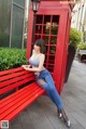 A woman sitting on a red bench in front of a red phone booth.